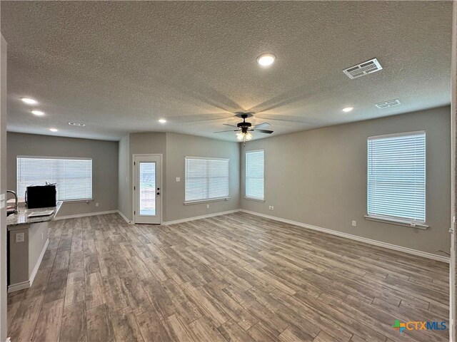 unfurnished living room with wood finished floors, a ceiling fan, visible vents, and a textured ceiling
