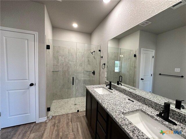bathroom with wood finished floors, visible vents, a sink, and a shower stall
