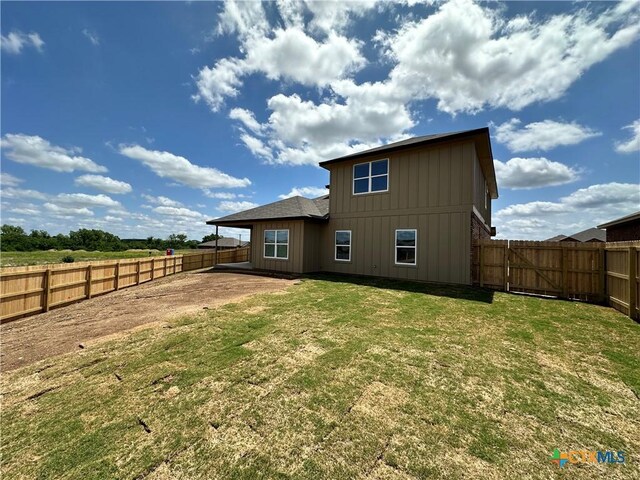 back of property with board and batten siding, a fenced backyard, and a yard