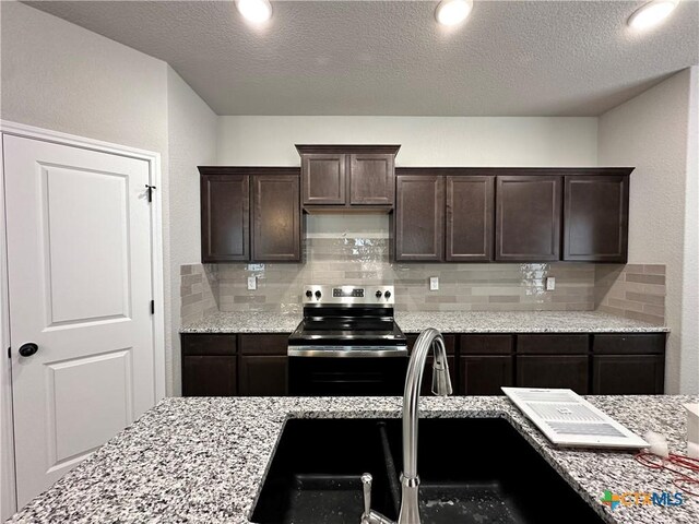 kitchen with backsplash, a sink, light stone countertops, dark brown cabinetry, and stainless steel electric range