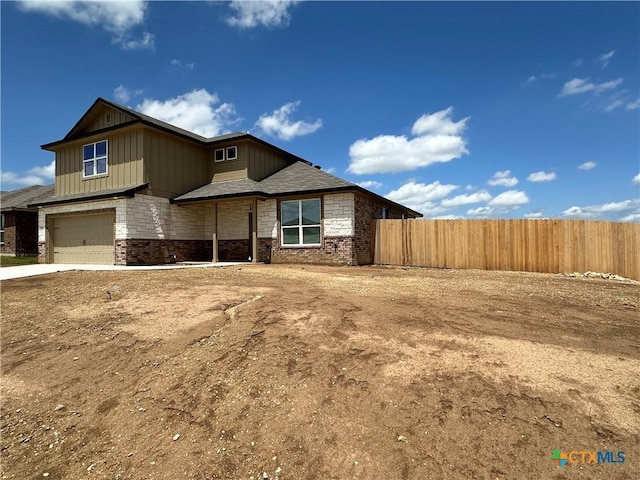 view of front of home featuring a garage, driveway, brick siding, and fence