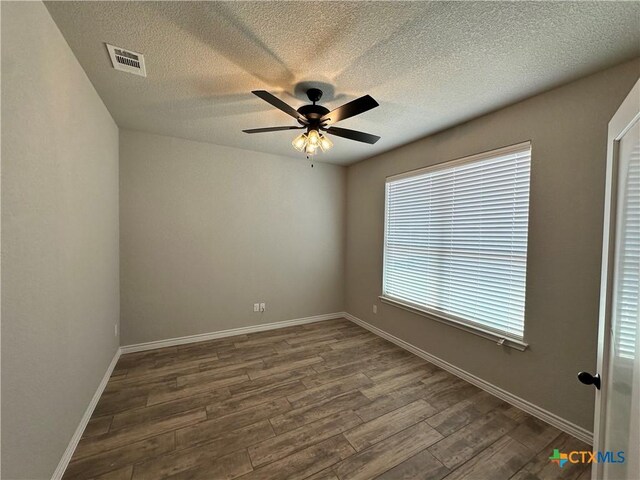 spare room featuring a textured ceiling, dark wood-style flooring, baseboards, visible vents, and a ceiling fan