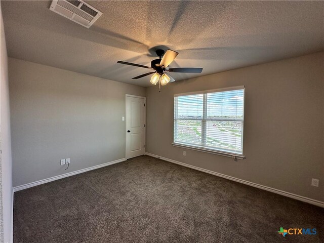 empty room with a ceiling fan, a textured ceiling, dark carpet, baseboards, and visible vents
