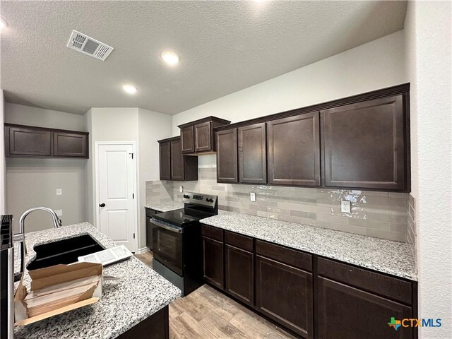 kitchen with a sink, stainless steel electric range oven, dark brown cabinets, visible vents, and decorative backsplash