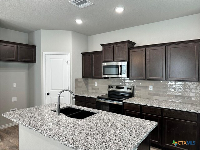 3005 Hedwig St, Killeen, TX 76549 - kitchen with appliances with stainless steel finishes, a sink, wood finished floors, dark brown cabinetry, and decorative backsplash