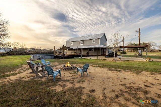 rear view of property with an outdoor fire pit, an outdoor pool, a patio area, a lawn, and metal roof