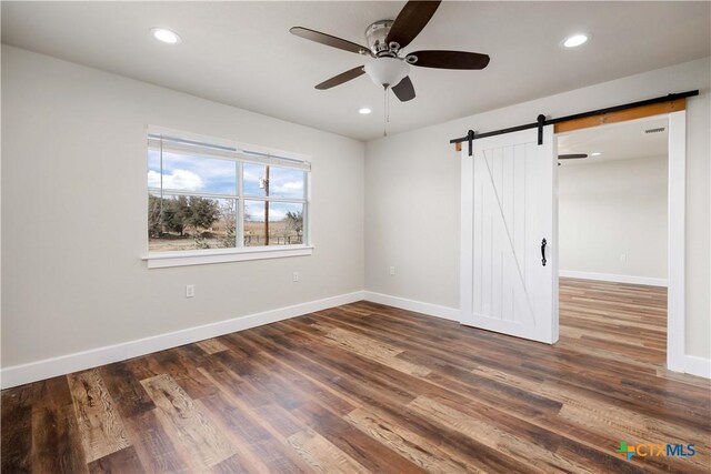 spare room with recessed lighting, a barn door, and wood finished floors