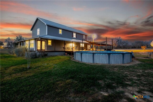 back of house with an outdoor pool, metal roof, and a lawn