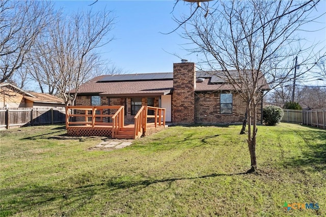 back of house with a wooden deck, a lawn, and solar panels