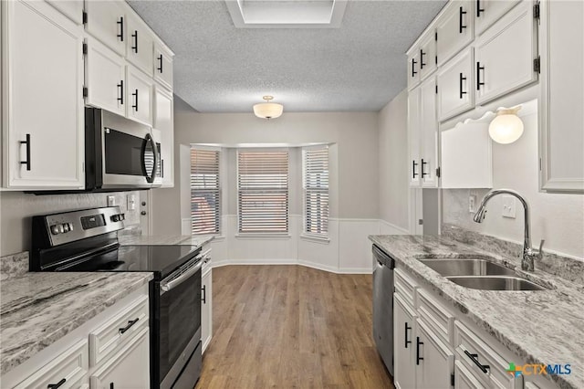 kitchen with sink, white cabinets, stainless steel appliances, a textured ceiling, and light hardwood / wood-style flooring