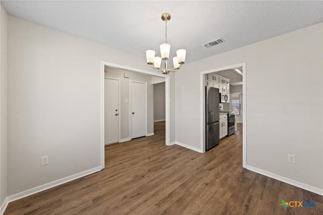 unfurnished dining area with dark hardwood / wood-style flooring, a notable chandelier, and a textured ceiling