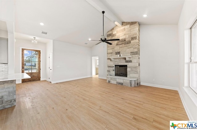 unfurnished living room featuring a stone fireplace, light hardwood / wood-style flooring, lofted ceiling with beams, and ceiling fan with notable chandelier