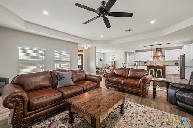 living room with hardwood / wood-style flooring, ceiling fan, and a raised ceiling