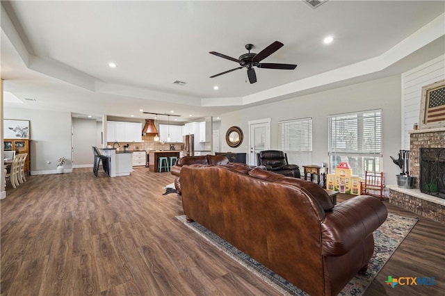 living room with a fireplace, ceiling fan, a raised ceiling, and dark wood-type flooring