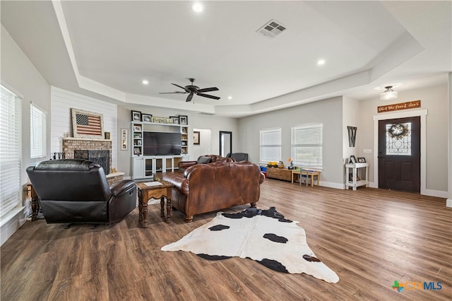 living room featuring ceiling fan, a brick fireplace, dark hardwood / wood-style floors, and a raised ceiling