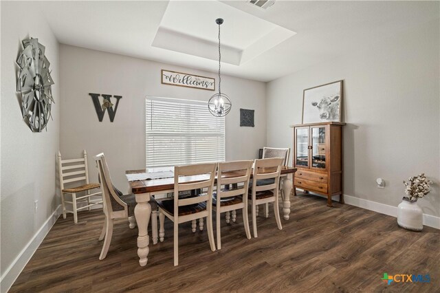 dining space featuring dark wood-type flooring, a raised ceiling, and an inviting chandelier