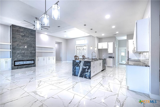 kitchen with white cabinets, sink, hanging light fixtures, ceiling fan, and a tiled fireplace