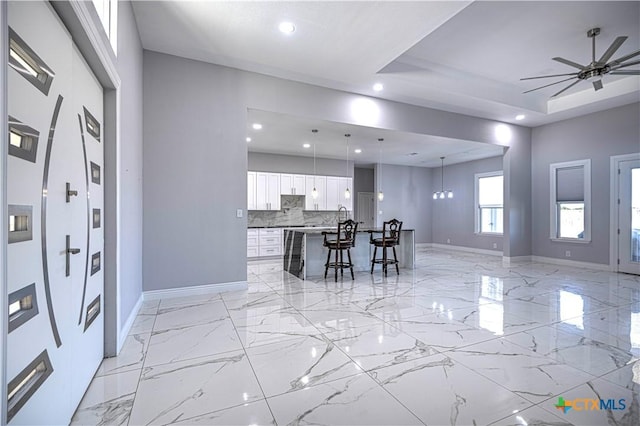 kitchen with a kitchen breakfast bar, a raised ceiling, pendant lighting, a center island, and white cabinetry