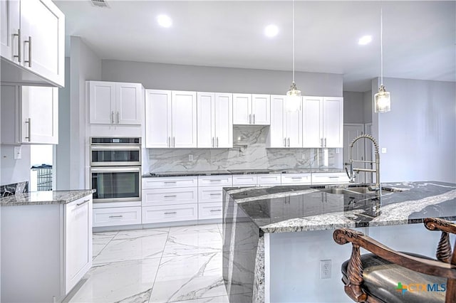 kitchen with hanging light fixtures, sink, double oven, light stone counters, and white cabinetry