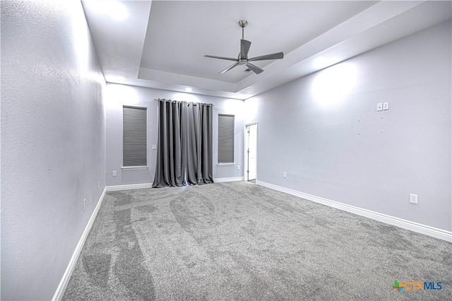 spare room with a tray ceiling, ceiling fan, and carpet