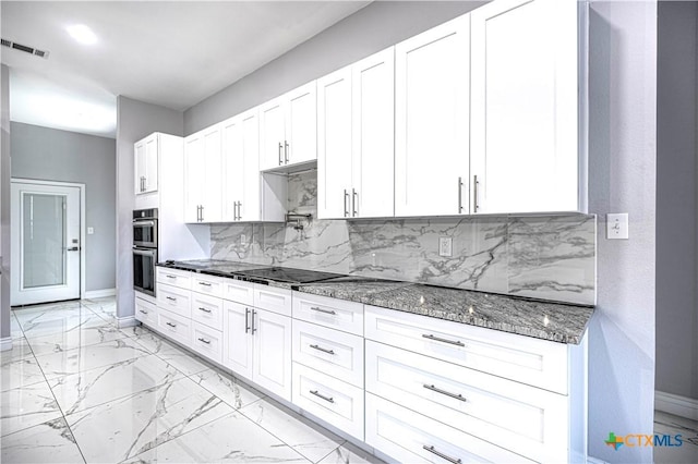 kitchen with tasteful backsplash, dark stone counters, stainless steel double oven, black electric cooktop, and white cabinetry