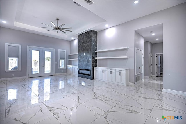 unfurnished living room featuring french doors, a raised ceiling, built in shelves, ceiling fan, and a fireplace