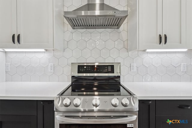 kitchen featuring white cabinets, wall chimney range hood, stainless steel stove, and tasteful backsplash