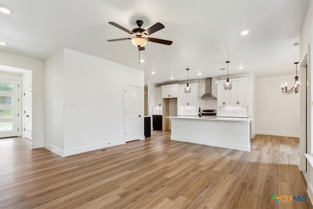 unfurnished living room featuring light wood-type flooring, sink, and ceiling fan with notable chandelier