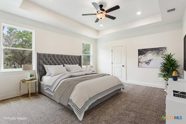 bedroom with multiple windows, ceiling fan, and a tray ceiling