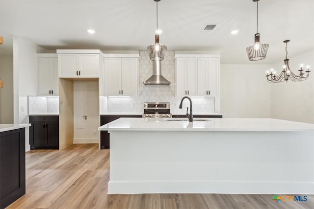 kitchen featuring stainless steel stove, hanging light fixtures, light hardwood / wood-style floors, white cabinets, and a kitchen island with sink