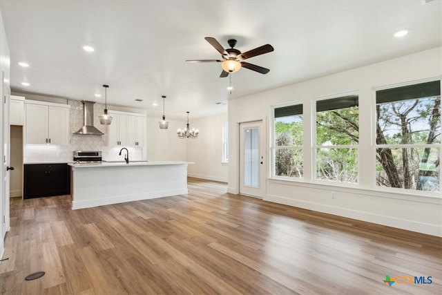 unfurnished living room featuring ceiling fan with notable chandelier and light hardwood / wood-style flooring