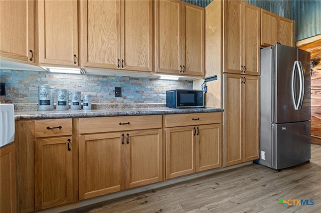 kitchen featuring black microwave, light wood finished floors, backsplash, and freestanding refrigerator