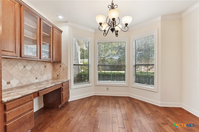 unfurnished dining area featuring a notable chandelier, built in desk, dark hardwood / wood-style floors, and ornamental molding