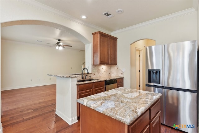 kitchen with light stone countertops, stainless steel appliances, sink, wood-type flooring, and a center island