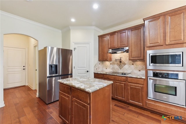 kitchen with light stone countertops, appliances with stainless steel finishes, ornamental molding, a center island, and dark hardwood / wood-style floors