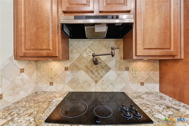 kitchen featuring decorative backsplash, light stone countertops, black electric stovetop, and extractor fan