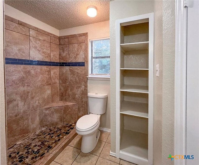 full bath featuring a textured ceiling, toilet, a tile shower, tile patterned floors, and a textured wall