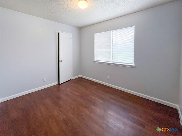 empty room with dark wood finished floors, a textured ceiling, and baseboards