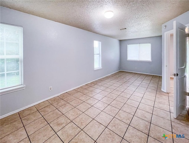 spare room with a textured ceiling, light tile patterned flooring, and baseboards