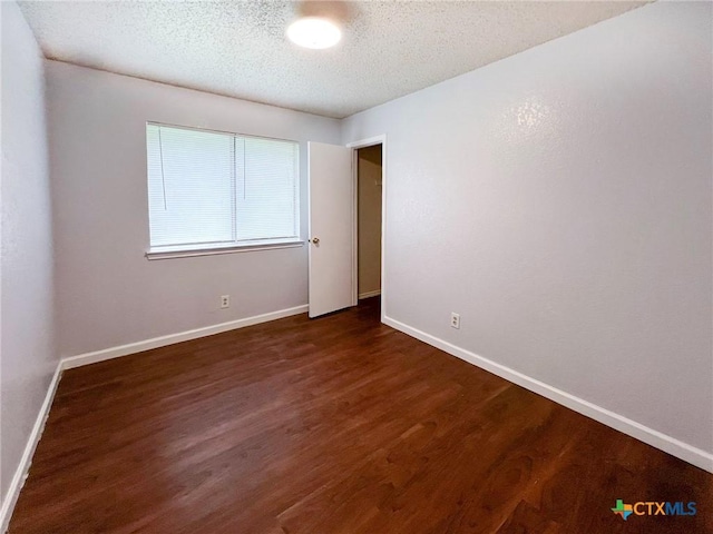 unfurnished room with dark wood-type flooring, a textured ceiling, and baseboards