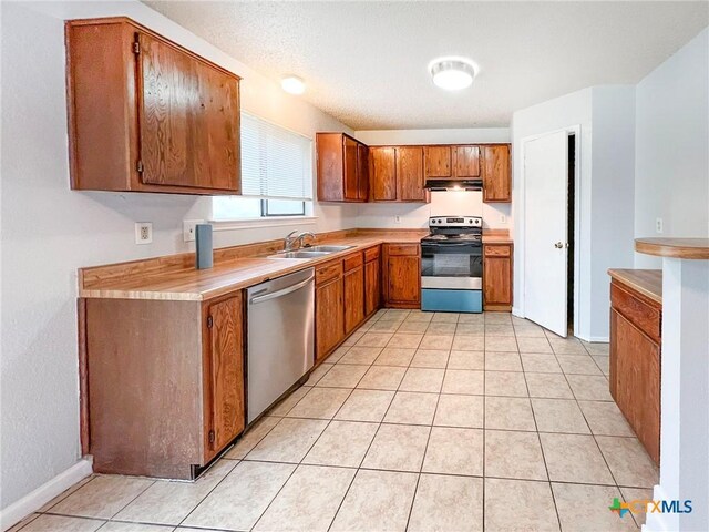 kitchen with appliances with stainless steel finishes, a sink, brown cabinetry, light countertops, and under cabinet range hood