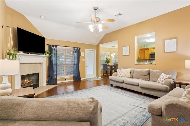 living room with a tiled fireplace, ceiling fan, hardwood / wood-style floors, and lofted ceiling