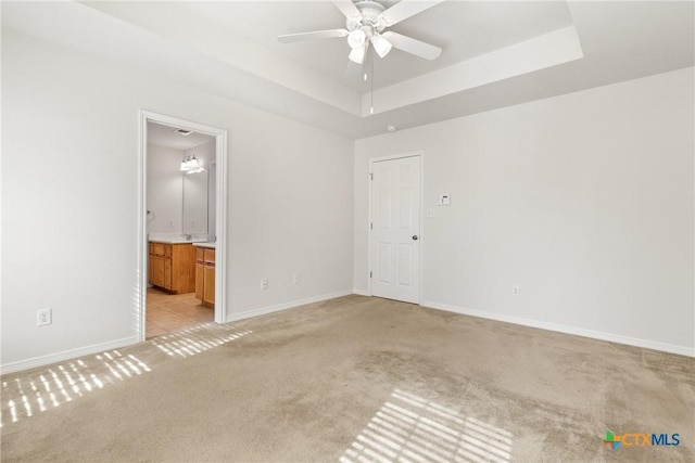 empty room with a tray ceiling, light colored carpet, and ceiling fan