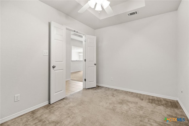 unfurnished bedroom with light carpet, a raised ceiling, and ceiling fan