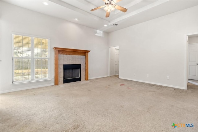 unfurnished living room with a raised ceiling, a tile fireplace, light colored carpet, and ceiling fan