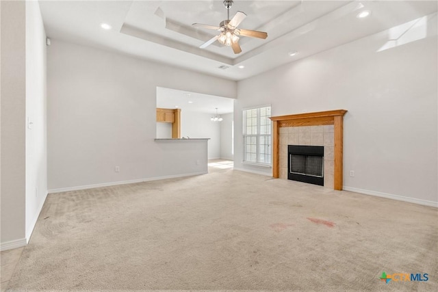 unfurnished living room with ceiling fan with notable chandelier, a fireplace, a tray ceiling, and light colored carpet