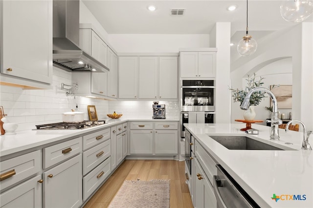 kitchen with visible vents, light wood finished floors, stainless steel appliances, a sink, and wall chimney range hood