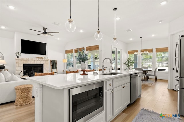 kitchen featuring open floor plan, light countertops, a stone fireplace, appliances with stainless steel finishes, and a sink