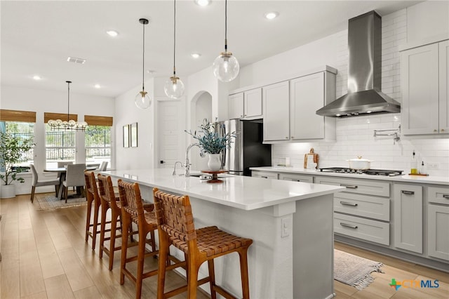 kitchen with gas cooktop, visible vents, freestanding refrigerator, a sink, and wall chimney range hood