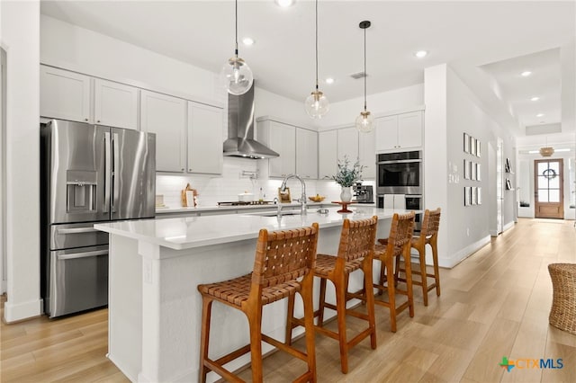 kitchen with tasteful backsplash, light countertops, appliances with stainless steel finishes, wall chimney exhaust hood, and a sink